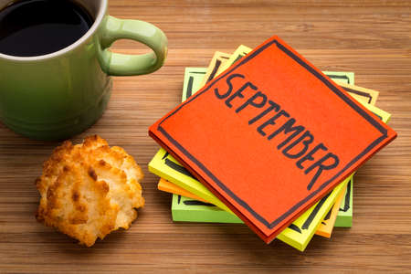 September  - handwriting in black ink on a  sticky note with a cup of coffee and cookieの写真素材