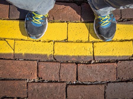 Waiting behind a yellow line - man's feet on a train station platform