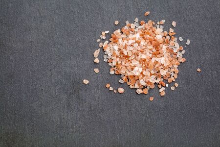 background of Himalayan salt - a heap of pink and orange coarse crystals on slate stone with a copy...