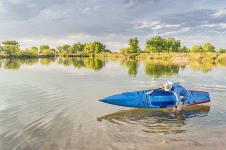 Male senior paddler rinsing his stand up paddleboard on a lake, late summer scenery in northern Coloradoの写真素材