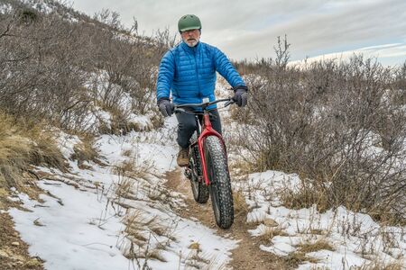 a senior male riding a fat bike on Cheyenne Rim in Red Mountain Open Space, late fall or winter scenery with some snowの写真素材