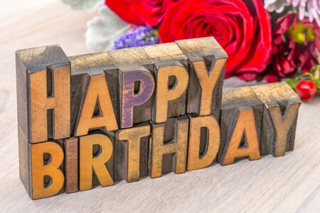 Happy Birthday greeting card in vintage letterpress wood type against grained wood with flowersの写真素材