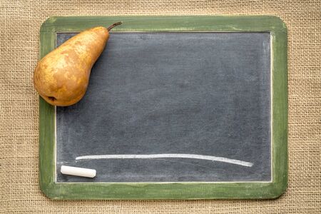blank slate blackboard with a pear and white chalk against burlap canvasの写真素材