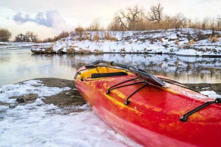 winter kayaking in Colorado - red whitewater kayak with a paddle on shore of St Vrain Creekの写真素材