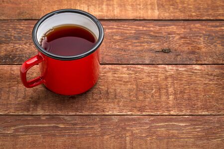 red metal cup of hot tea on a rustic wooden picnic table with a copy spaceの写真素材