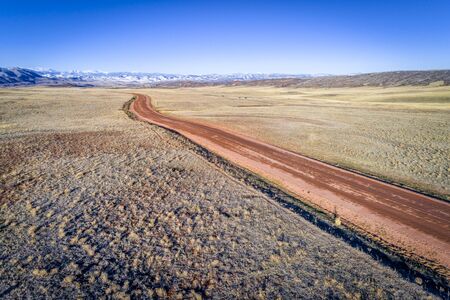 Road across Colorado foothills with snowy Rocky Mountains in background, winter or early spring...