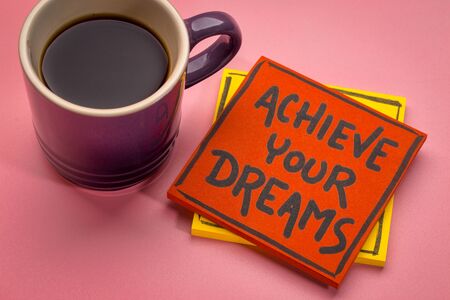 achieve your dreams reminder  handwriting on a sticky note wit a cup of coffeeの写真素材