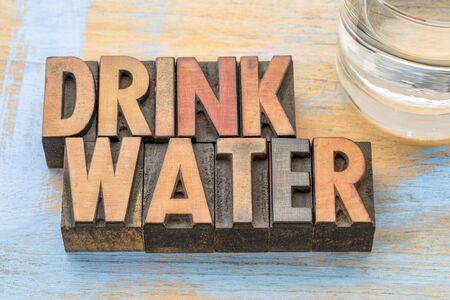 drink water advice - word abstract in vintage letterpress wood type with a glass of water