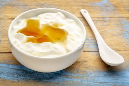 Live organic Greek yogurt with natural honey in a white ceramic bowl against grunge wood, top viewの写真素材