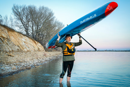 Fort Collins, CO, USA - April 22, 2018: Senior paddler is launching his racing stand up paddleboard (2018 All Star by Starboard) for an evening lake workout.のeditorial素材