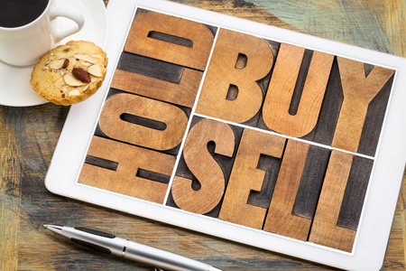 buy, hold, sell - investing concept - word abstract in vintage letterpress wood type on a digital tablet with a cup of coffeeの写真素材