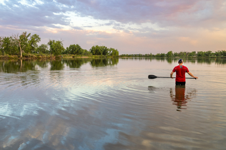 Male paddler with a long stand up paddle standing in a calm lake, summer scenery