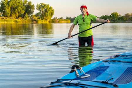 Environmental portrait of a senior male paddler with a stand up paddleboard on a calm lake in northern Colorado, summer sceneryの写真素材