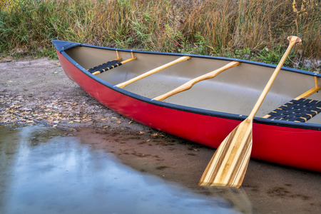 red tandem canoe with a wooden paddle on a lake shore