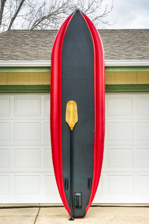 whitewater inflatable stand up paddleboard with a paddle leaned against house wallの写真素材