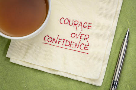 Courage over confidence doodle - handwriting on a napkin with cup of teaの写真素材
