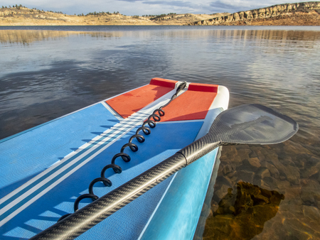 Stand up paddleboard with a paddle and safety leash on a mountain lake in winter.の写真素材