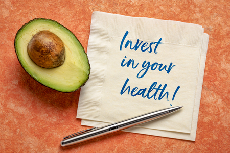 invest in your health - handwiring on napkin with a cut avocado against bark paper