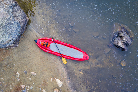 inflatable whitewater stand up paddleboard on a shore of mountain river - Poudre River in Colorado,...