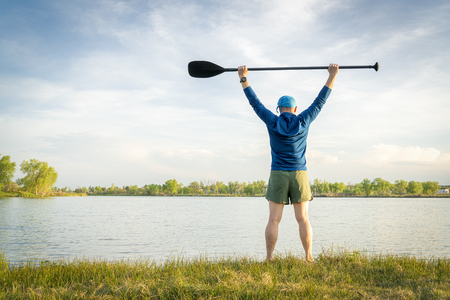 mature stand up paddler is stretching and warming up on a lake shore before paddling workoutの写真素材