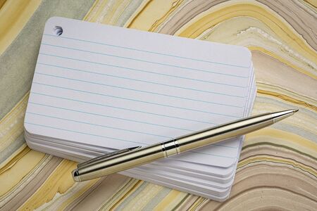 stack of blank index card with a pen over wavy marbled paperの写真素材