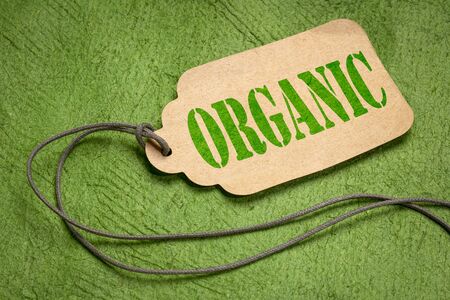 organic text  on a paper price tag with a twine against textured green bark paperの写真素材