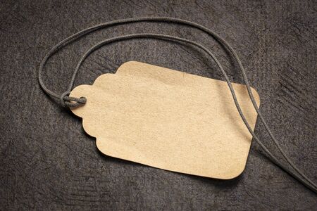 blank paper price tag with a twine against textured black bark paper