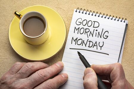 Good Morning Monday - man hand writing a note with a black marker in a spiral notebook, overhead view with a cup of coffeeの写真素材