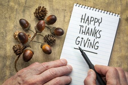 Happy Thanksgiving  greeting card - man hand writing a note with a black marker in a spiral notebook with acorn and cone decorationの写真素材