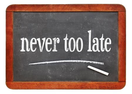 never too late - white chalk reminder text on a vintage slate blackboardの写真素材