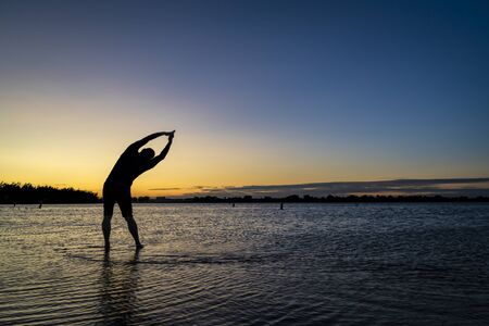 practicing yoga palm tree pose - sunrise silhouette of a man on a lake beach, Boyd Lake State Park...