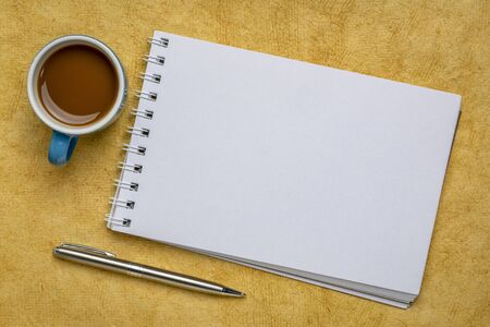blank spiral art sketchbook against yellow textured bark paper with a cup of coffeeの写真素材