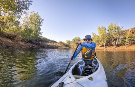 Senior male paddler is paddling an expedition decked canoe on a mountain lake in Colorado, POV from...