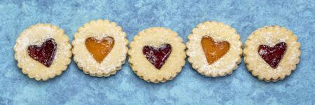 a row of jam heart biscuits on blue handmade textured bark paper, dessert or love and romance concept, panoramic bannerの写真素材