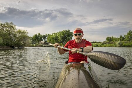 senior male paddler is paddling a long, narrow and fast racing sea kayak on  a calm lake, summer...