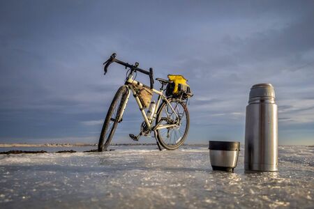 flask bottle and cup of hot tea on an icy lake shore during winter biking, Boyd Lake State Park in northern Coloradoの写真素材
