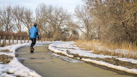 male rider is commuting on electric skateboard along bike trail in winter scenery in northern Colorado - Colorado Front Range Trail in Boyd Lake State Parkの写真素材