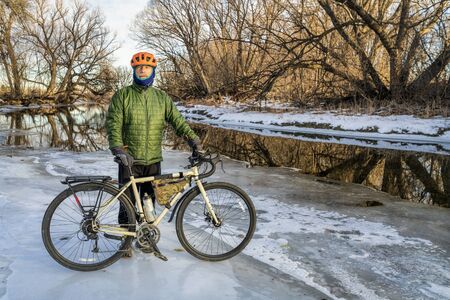senior male cyclist with a touring bike on an icy river shore, Poudre River in Fort Collins, Colorado, winter biking or commuting conceptの写真素材