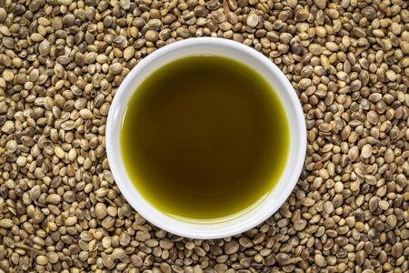 hemp seed oil in a small ceramic bowl against a background of dry hemp seedsの写真素材