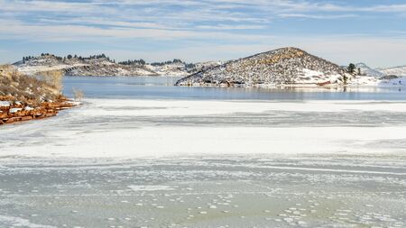 Partially frozen calm lake at foothills of Rocky Mountains - Horsetooth Reservoir, a popular recreation destination near Fort Collins in northern Colorado, winter scenery.の写真素材
