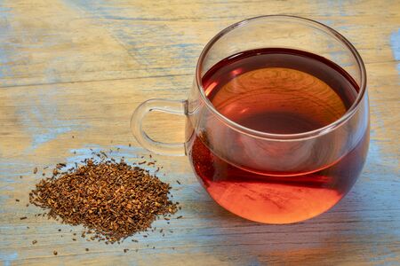 rooibos red tea  -  a glass cup of a hot drink and loose leaves, tea made from the South African red bush, naturally caffeine freeの写真素材