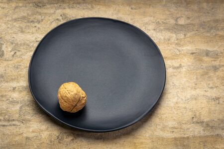 Single walnut on a black plate against textured bark paper. Food abstract with a copy space.の写真素材