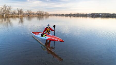 senior male paddler in a drysuit and life jacket is finishing his workout with a long racing stand...
