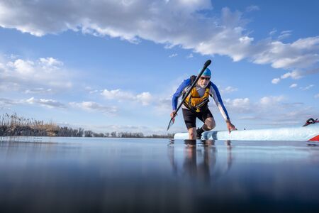 senior male paddler with his stand up paddleboard on a shore of calm lake, low angle view form...