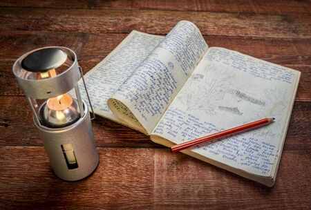 Vintage expedition journal on a picnic table with a candle lantern. Travel log from paddling trip across north eastern Poland in August 1974 - handwriting and drawing in pencil. .の写真素材