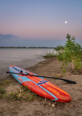 Loveland, CO, USA - July 2, 2020: Downwind stand up paddleboard (17.6' Interceptor by Mistral) on a beach at Boyd Lake State Park at dusk after paddling workout.のeditorial素材
