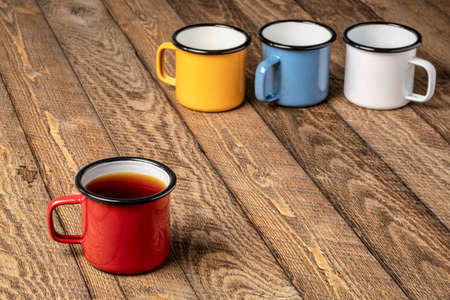 red metal cup of hot tea on a rustic wooden picnic table with a copy space and more cups in...