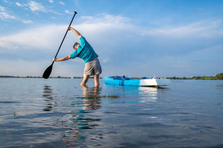 senior paddler is stretching and warming up before morning workout on a stand up paddleboard - Boyd...