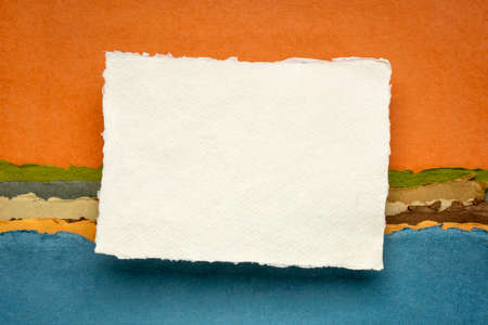 small sheet of blank white Khadi rag paper from South India with a metal pen against colorful...