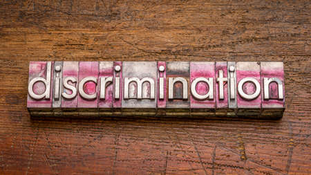 discrimination word abstract in gritty,  vintage letterpress metal type stained by printing ink against rustic, weathered wood, social issue conceptの写真素材